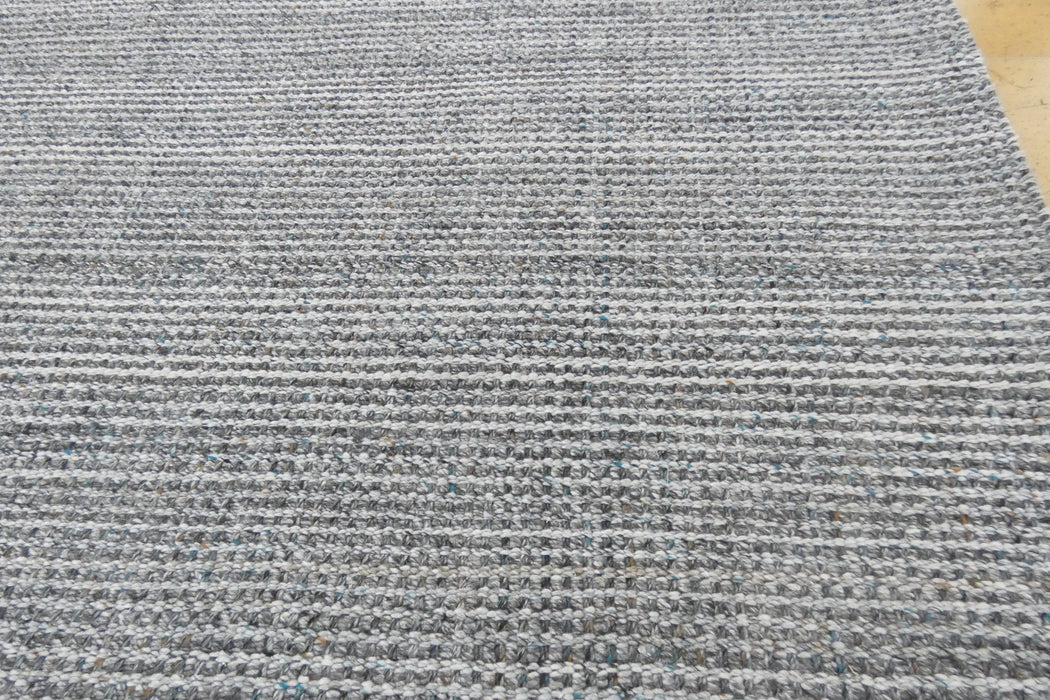 Close-up of a woven rug or textile with a heathered gray and white striped pattern, showing the texture and weave detail.