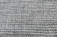 A close-up of a woven rug or mat with a textured, chunky pattern in heathered gray, white, and black, with subtle hints of blue and brown threads.