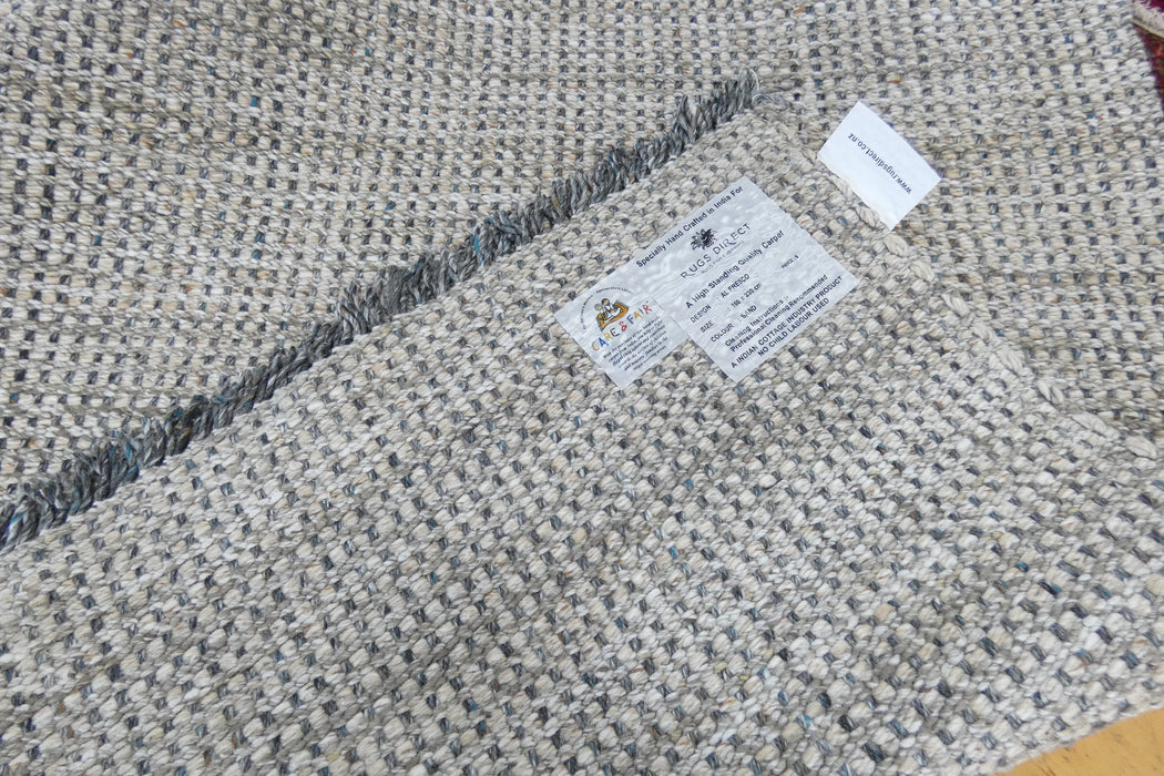 Close-up of a woven area rug with a textured pattern of beige, gray, and white threads, showing a white product label and a small white tag.