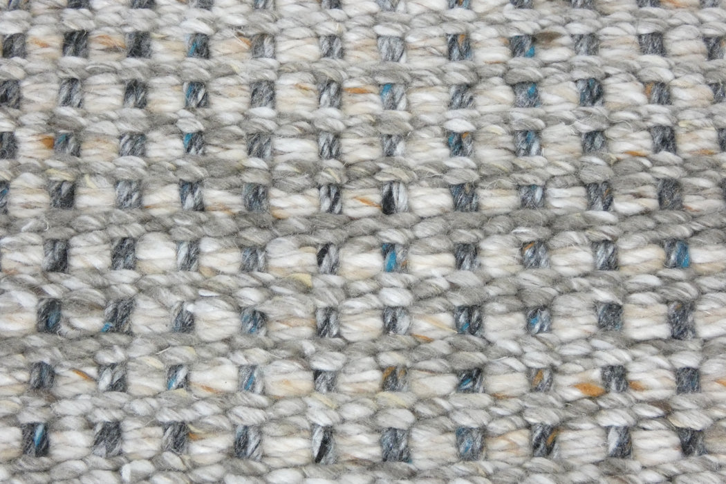 Close-up of a woven textile surface with a basketweave pattern in off-white, gray, and small blue and tan flecks.