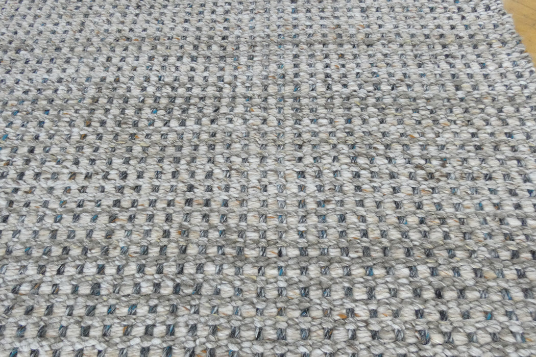A close-up of a woven rug or mat with a textured pattern of gray, white, and black fibers.
