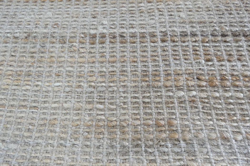A close-up of a woven natural fiber rug or mat with a textured grid pattern in beige, cream, and light brown tones.