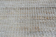 A close-up of a woven natural fiber rug or mat with a textured grid pattern in beige, cream, and light brown tones.