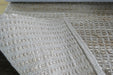 A close-up of a woven area rug with a textured, basketweave pattern in cream and light tan tones.