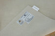 A close-up of a light beige woven fabric product, likely a rug or mat, showing a white sewn-in label and a hanging product tag. The tag reads 'BROOKFIELD HOME FURNITURE' and 'AUSTRALIA'.