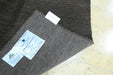 A folded dark brown wool fabric sample with two white labels attached, placed on a light beige tiled floor.