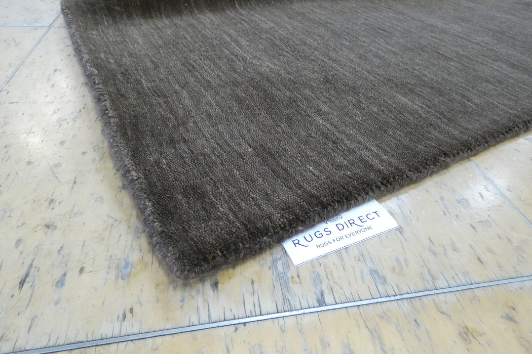 A close-up of a dark brown textured rug corner with a white 'RUGS DIRECT' label, placed on a light-colored wooden floor.