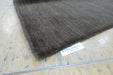 A close-up of a dark brown textured rug corner with a white 'RUGS DIRECT' label, placed on a light-colored wooden floor.