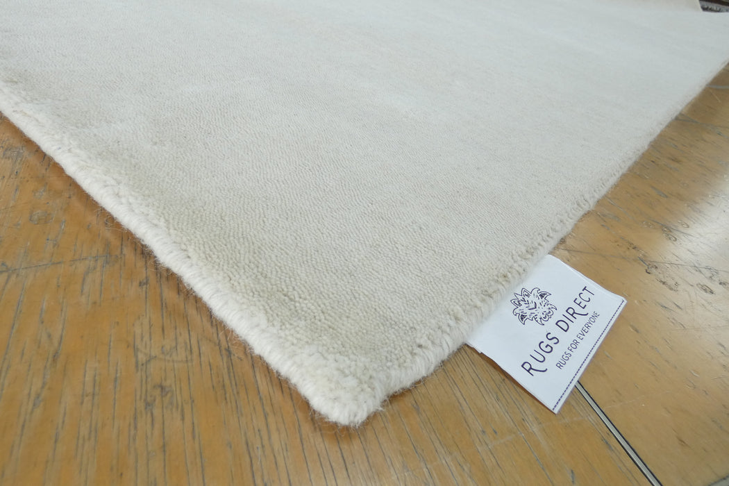A close-up of a cream-colored plush rug corner with a white 'RUGS DIRECT' brand tag, placed on a light brown wooden floor.