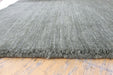 A close-up of a textured gray woven rug with a frayed edge, laid on a light-colored wooden floor.