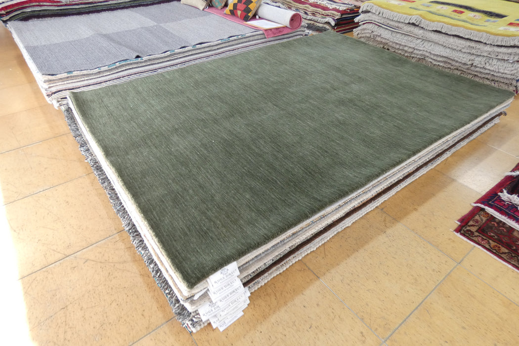 A stack of rectangular area rugs displayed on a tiled floor, with the top rug in olive green and fringed edges visible around the sides.