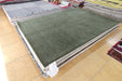 A stack of rectangular area rugs displayed on a tiled floor, with the top rug in olive green and fringed edges visible around the sides.