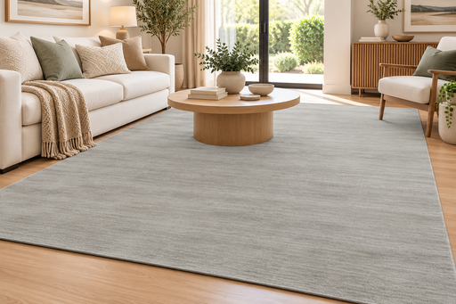 A large light gray area rug with a subtle textured pattern, styled in a bright, modern living room with a beige sofa, wooden coffee table, and light wood flooring.