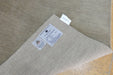 A close-up of a woven beige rug or textile corner with two product labels attached, photographed on a light wood surface.