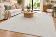 A large off-white textured area rug in a modern, sunlit living room with a white sofa, wooden coffee table, and light wood flooring.