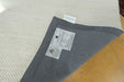 A gray woven area rug shown from above, folded over at one corner to reveal the underside and a brand label. The underside is heather gray, and the top surface is a textured cream/off-white.