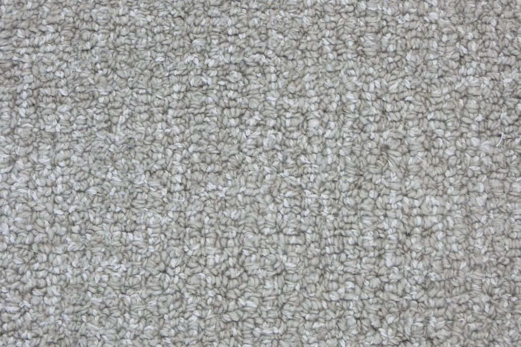 A close-up texture shot of a loop pile carpet in a light warm gray or greige color.