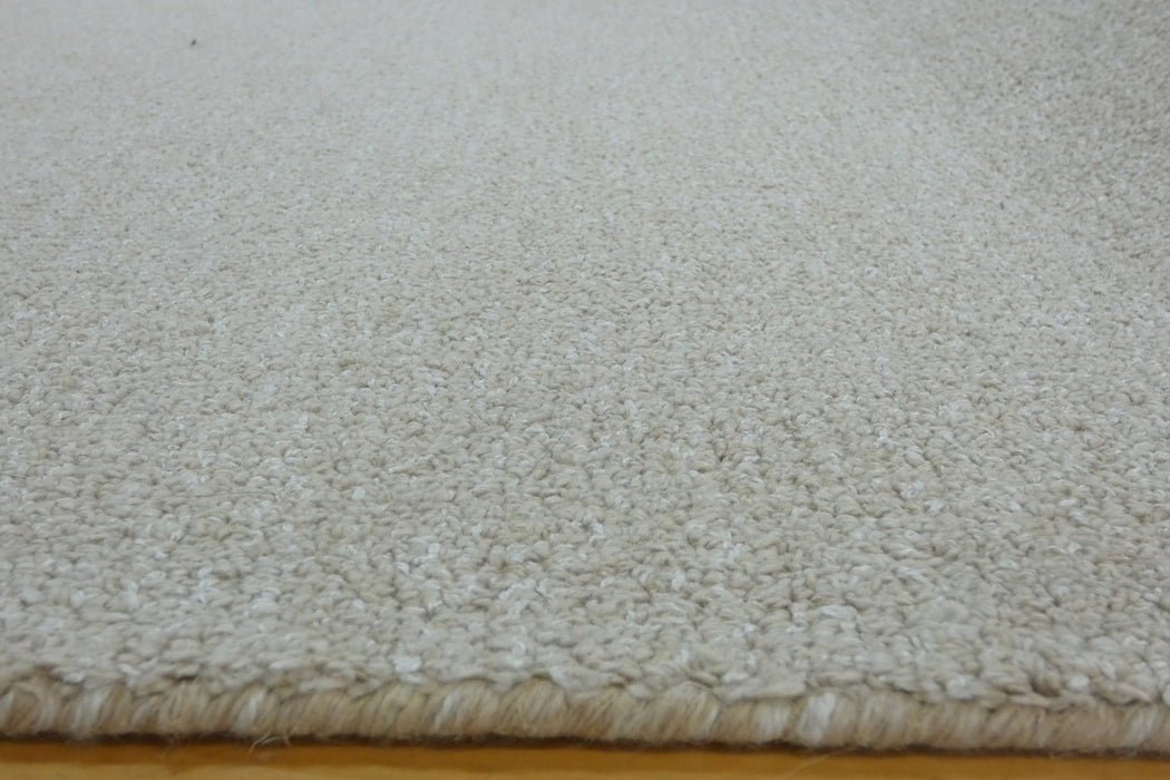Close-up of a textured off-white or cream shag rug, showing the pile height and the frayed edge resting on a wooden floor.