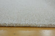 Close-up of a cream-colored shag rug with a thick textured pile and fringed edge, shown resting on a light wood floor.