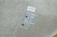 Close-up of a woven off-white rug corner showing two sewn-in labels, including a circular logo that appears to read 'The Rug Club' and a small white tag above it.