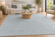 A large light blue textured area rug in a modern living room setting with a wooden coffee table, beige sofa, and potted plants.
