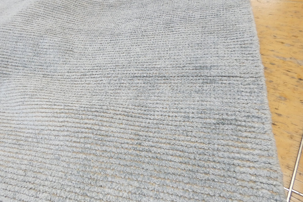 A close-up of a light gray ribbed fabric or carpet texture, with a small portion of a yellow surface visible at the right edge.