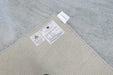 Close-up of the corner of a woven area rug showing the backing, product labels, and the adjacent light gray textured rug surface.