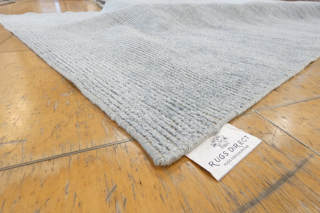 A close-up of a light gray ribbed rug laid on a polished wooden floor, with a white fabric tag reading 'RUGS DREIST' attached near one corner.