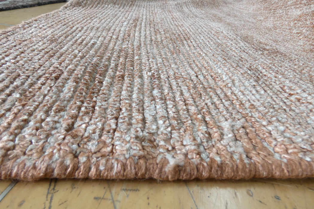 A close-up of a thick, textured woven rug in a blend of dusty pink, beige, and white fibers, laid out on a light-colored wooden floor.