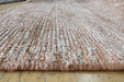 A close-up of a thick, textured woven rug in a blend of dusty pink, beige, and white fibers, laid out on a light-colored wooden floor.