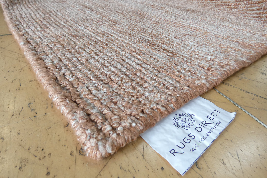 A close-up of a textured woven rug corner on a wooden floor, with a white fabric tag reading RUGS DIRECT visible along the edge.