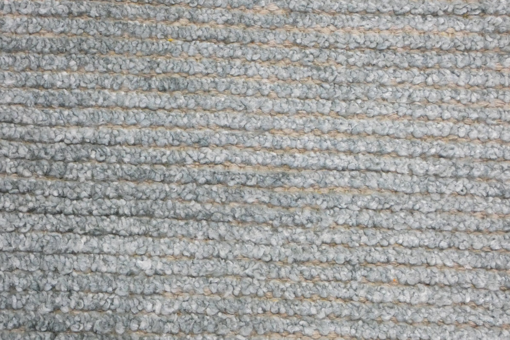 A close-up of a gray looped carpet or rug texture with horizontal ribbed rows and subtle beige gaps between the fibers.