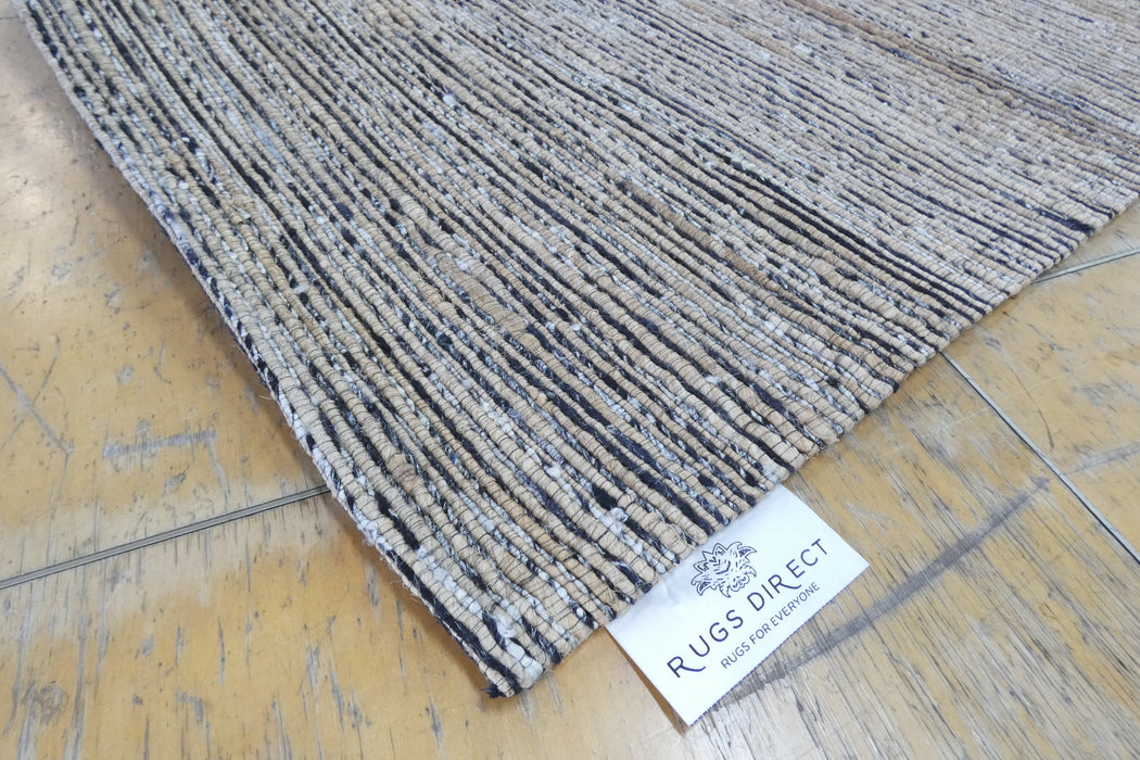 A close-up of a textured woven rug corner on a light wood floor, with a white tag reading RUGS DIRECT visible near the edge.