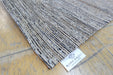 A close-up of a textured woven rug corner on a light wood floor, with a white tag reading RUGS DIRECT visible near the edge.