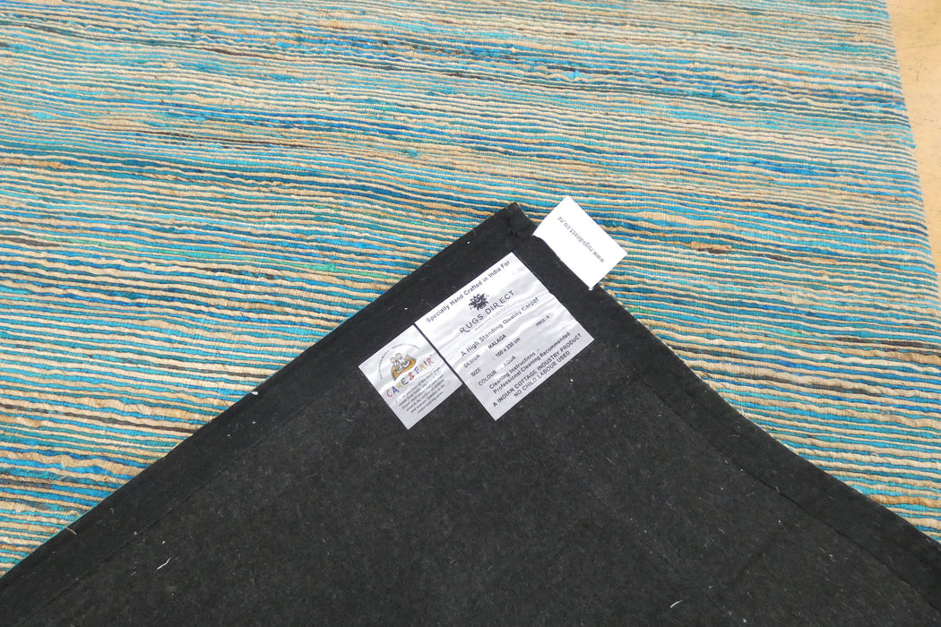 A close-up of the corner of a black rug or mat showing two white product labels, placed over a blue and tan striped rug that serves as the background.