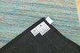 A close-up of the corner of a black rug or mat showing two white product labels, placed over a blue and tan striped rug that serves as the background.