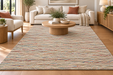 A large rectangular area rug with a textured, multicolored horizontal stripe pattern in beige, blue, red, and brown tones, styled in a bright, modern living room with a light wood coffee table and a cream sofa.