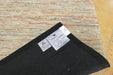 A close-up of a dark charcoal gray carpet sample or rug backing laid on top of a multicolored woven rug, with two product labels visible.