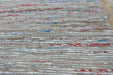 A close-up of a woven textile or rug with horizontal natural-fiber stripes in beige, white, and small scattered red and blue accents.