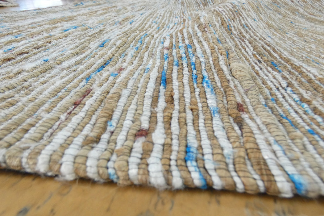 A close-up of a woven natural fiber rug with vertical stripes in beige, white, and small blue accents, resting on a wooden floor.