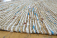 A close-up of a woven natural fiber rug with vertical stripes in beige, white, and small blue accents, resting on a wooden floor.