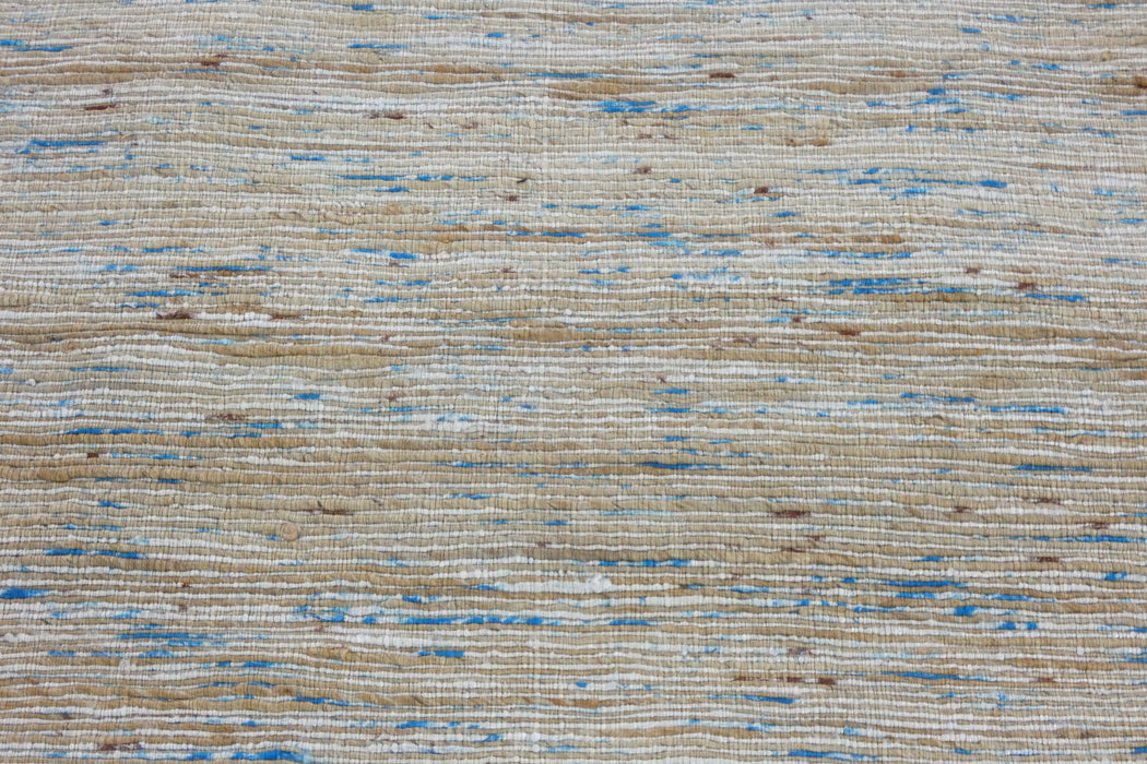 A close-up of a woven rug or textile with a textured horizontal pattern in natural beige, cream, and light blue.