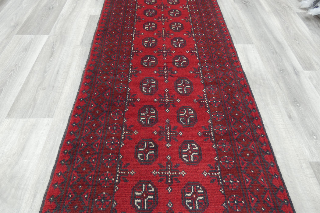 Red Afghan Turkman Bokhara hand-knotted wool hallway runner featuring repeating oval Gul medallions and traditional geometric borders. Rugs Direct NZ