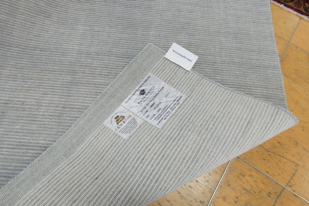 A close-up of a light gray ribbed fabric or rug corner with two labels attached, laid over a tan tiled floor.