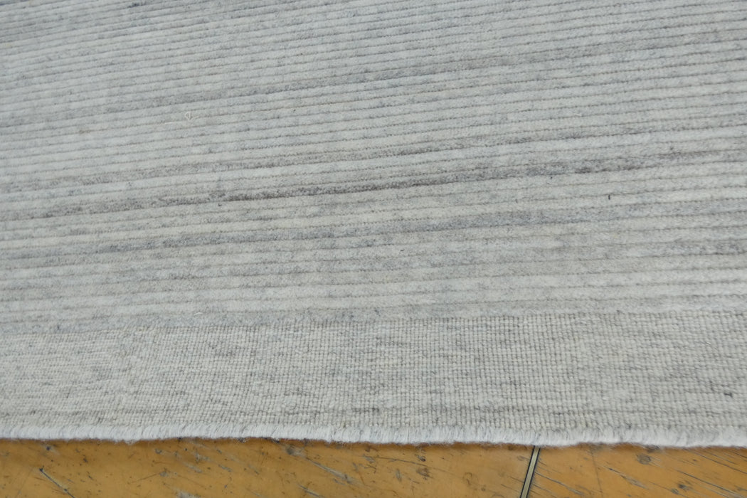 Close-up of a light gray textured rug with horizontal ribbed stripes, shown on a wooden floor.