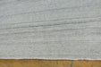 Close-up of a light gray textured rug with horizontal ribbed stripes, shown on a wooden floor.