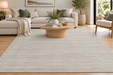 A large rectangular area rug in a light beige-gray tone with a subtle horizontal textured pattern, shown in a modern living room setting with a wooden coffee table, beige sectional sofa, and light wood flooring.