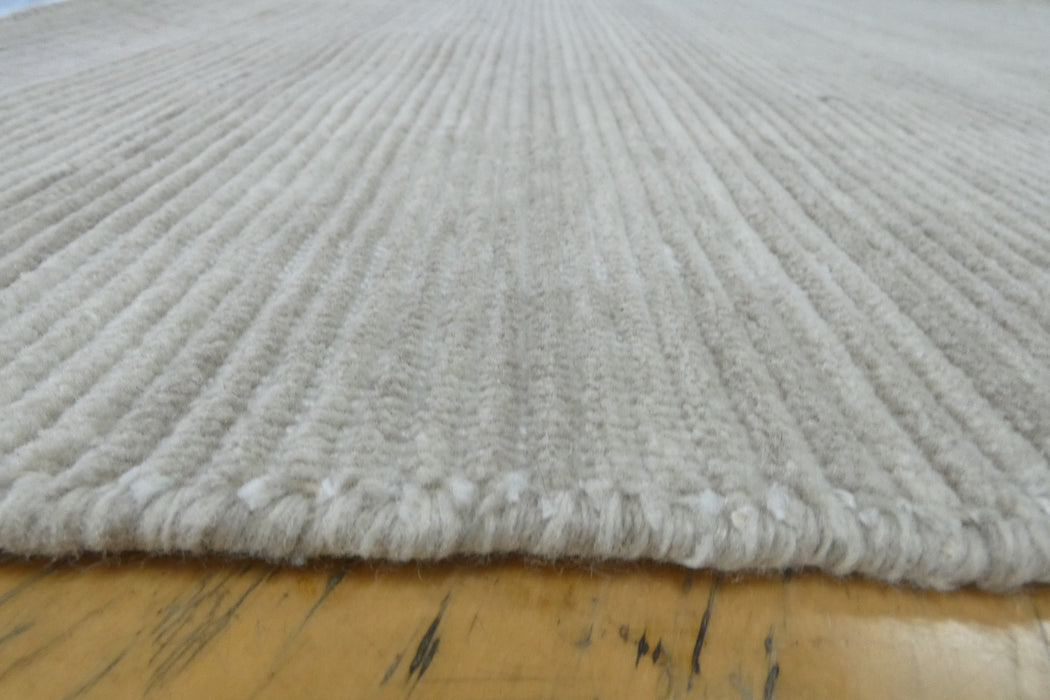 Close-up of a textured off-white or cream area rug with a ribbed pattern, shown resting on a light-colored wooden floor.