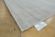 A close-up of a light beige textured rug corner with a white 'RUGS DIRECT' brand tag, laid on a light brown wooden floor.