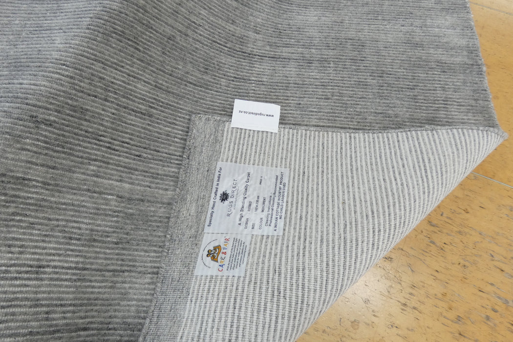 A close-up of a gray ribbed knit fabric, likely a blanket or throw, showing the underside with two labels. One label reads 'COTTON BLEACHED' and the other shows the 'COTTON CLUB' logo.